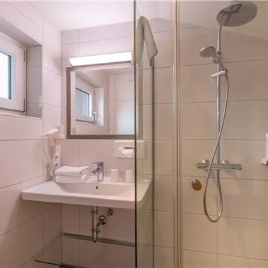 A modern bathroom with a glass shower cubicle and a sink. It is bright and well-lit with white tiles.