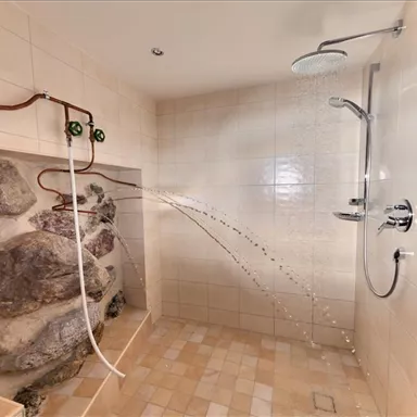 Eine moderne Dusche mit einem Felsdesign und zwei Wasserhähnen. Das Licht fällt sanft auf die gefliesten Wände und den Boden.