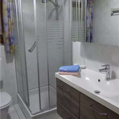 Ein modernes Badezimmer mit einer Duschkabine und einem Waschbecken. Die Wände sind hell gefliest und es gibt Holzschränke für Stauraum.