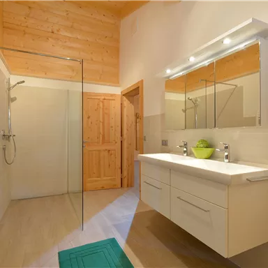 A modern bathroom with a large shower and a bright wooden ceiling. The sink area is elegant and well lit.