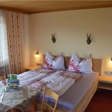 Ein gemütliches Schlafzimmer mit zwei Betten und rustikalem Holzdesign. Neben dem Bett stehen ein Tisch und Stühle, und die Wände sind mit dekorativen Elementen geschmückt.