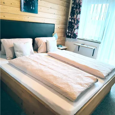 Ein einladendes Schlafzimmer mit einem großen Bett und hellen Kissen. Der Raum hat Holzverkleidungen und große Fenster, die viel Licht hereinlassen.