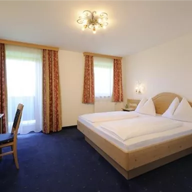 Ein gemütliches Schlafzimmer mit einem großen Doppelbett und Holzmöbeln. Das Zimmer hat große Fenster, die viel Tageslicht hereinlassen.