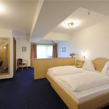 Ein gemütliches Hotelzimmer mit einem Doppelbett und modernem Holzdekor. Der Raum ist hell und freundlich, ausgestattet mit einem Tisch, einem Stuhl und einem Spiegel.