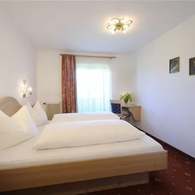 Ein gemütliches Schlafzimmer mit zwei Betten und einer hellen Fensterfront. Die Wände sind in neutralen Farben gehalten und die Einrichtung ist einfach und einladend.