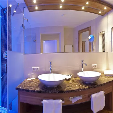 A modern bathroom with two sinks and an elegant shower. Bluish light creates a relaxed atmosphere.