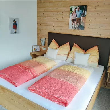 Ein gemütliches Schlafzimmer mit einem Doppelbett und bunten Bettdecken. Die Wände sind mit Holztäfelung und Bildern dekoriert.