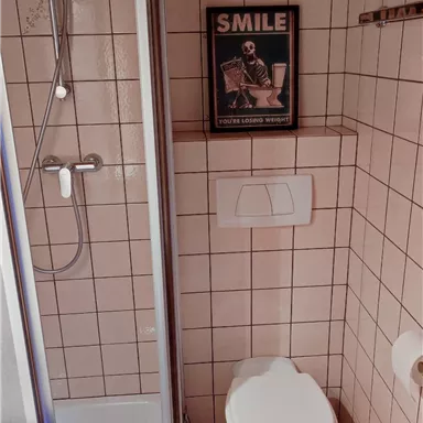 Ein kleines Badezimmer mit Dusche und Toilette. An der Wand hängt ein Poster mit der Aufschrift „SMILE“.