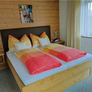 Ein gemütliches Schlafzimmer mit einem großen Doppelbett und bunten Kopfkissen. Das Holzdesign und das sanfte Licht schaffen eine einladende Atmosphäre.