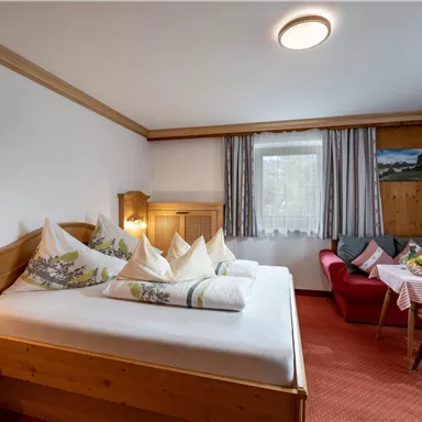 Ein gemütliches Zimmer mit einem Doppelbett und zwei Kissen. Angenehme Sitzecke und Fenster mit Blick ins Freie.