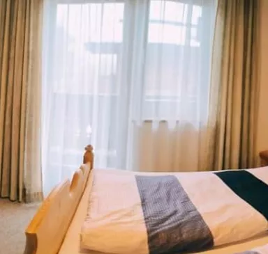 Ein gemütliches Zimmer mit zwei Betten, einem Tisch und Stühlen. Große Fenster sorgen für viel Tageslicht und eine einladende Atmosphäre.