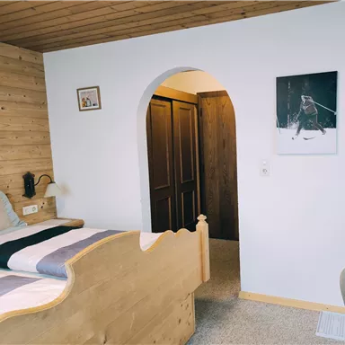 Ein gemütliches Schlafzimmer mit einem Holzbett und einer Holzverkleidung. Im Hintergrund befinden sich zwei Türen und ein Kunstwerk an der Wand.