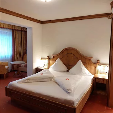 Ein gemütliches Schlafzimmer mit einem großen Holzbett und zwei Kissen. Die Wände sind in warmen Farbtönen gehalten und es gibt eine Fensterbank mit einer angenehmen Aussicht.