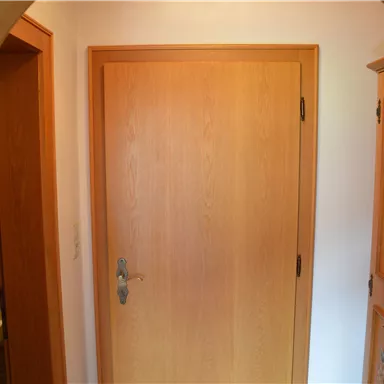 Ein heller Flur mit einer Holztür und einem Schrank. Auf der linken Seite ist ein Zugang zu einem Badezimmer sichtbar.