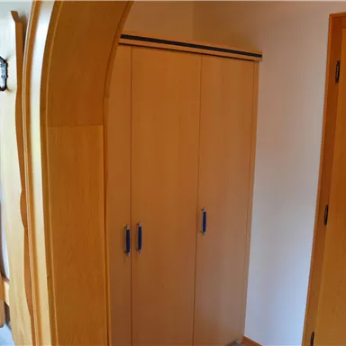 Ein einfacher Raum mit einem Holzschrank und einem offenen Regal. An der Wand hängen mehrere Kleiderhaken.