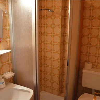 Ein kleines Badezimmer mit Dusche, Waschbecken und Toilette. Die Wände sind mit einem retro-musterartigen Tapete dekoriert.