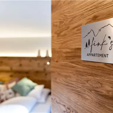 Ein modernes Appartement mit einem Holzschild, das "Link's Appartement" zeigt. Im Hintergrund sind gemütliche Kissen und ein warmes Licht sichtbar.