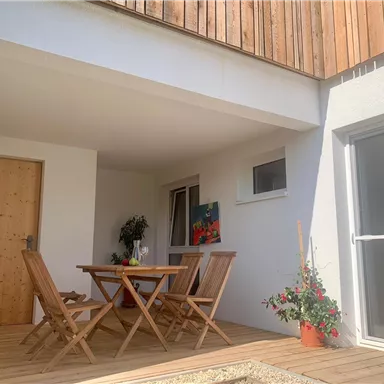 Ein einladender Außenbereich mit einem Holztisch und Stühlen. Die Terrasse ist hell und modern gestaltet, ideal zum Entspannen.
