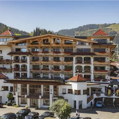 A beautiful hotel building in traditional alpine style. Surrounded by green mountains and blue sky.