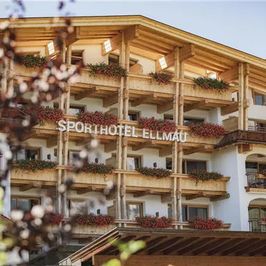 A modern sports hotel with a wooden facade and balconies adorned with flowers. The architecture is welcoming and friendly.