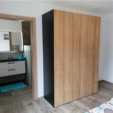 A modern bedroom with a large wooden closet. In the background, a bathroom can be seen.