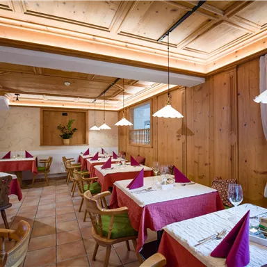 Ein gemütliches Restaurant mit Holzwänden und warmem Licht. Die Tische sind mit roten Tischdecken und Servietten dekoriert.