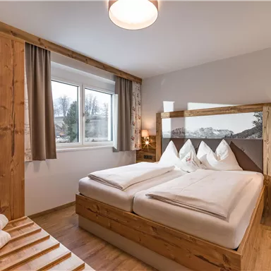 A cozy bedroom with wooden decor. It features a double bed, windows, and soft lighting.
