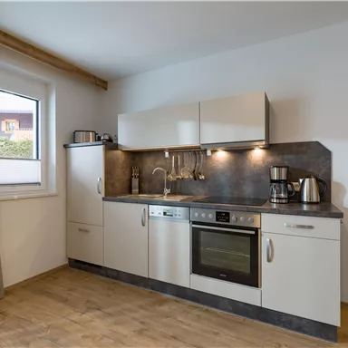 A modern kitchen with bright cabinets and an elegant countertop. It is well equipped with appliances such as a stove, dishwasher, and coffee maker.