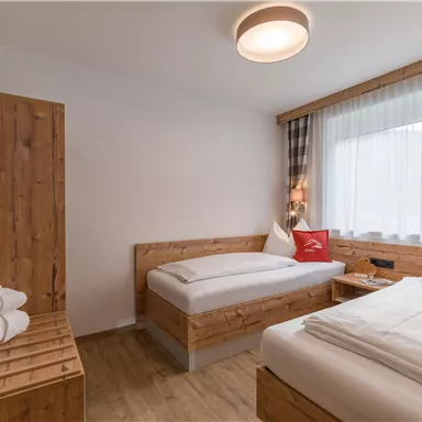 A modern hotel room with two wooden beds and a cozy atmosphere. There is a window with curtains and a television on the wall.