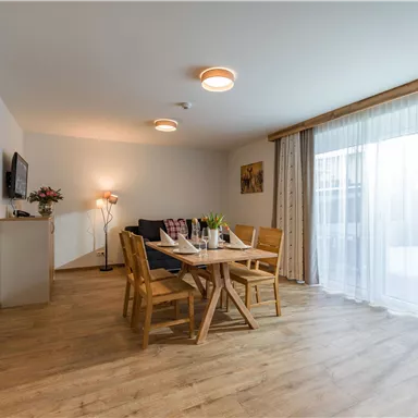 A bright and modern living room with a table and chairs. Large windows let in a lot of light and provide a view outside.