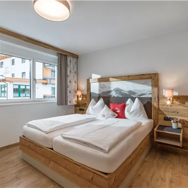A cozy bedroom with a double bed and wooden decor. Large windows let in plenty of light and offer a view of the surroundings.