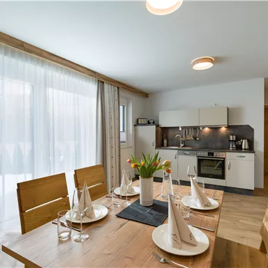 A modern kitchen with a wooden dining area. The table is beautifully set and there are large windows that let in plenty of light.