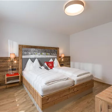A modern bedroom with a wooden double bed and white bedcovers. Warm light sources and subtle colors create an inviting atmosphere.