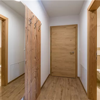 A bright hallway with brown wooden doors and a modern bathroom in the background. Coat hooks hang on the wall.