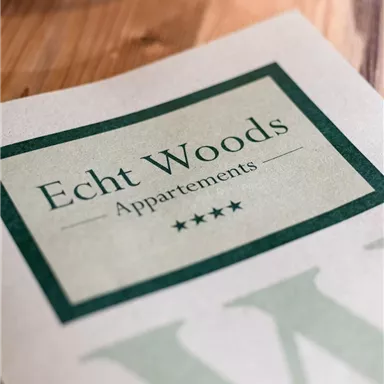A stylish leaf with the inscription "Real Woods Apartments" and four stars. The background is light and features a wood surface.