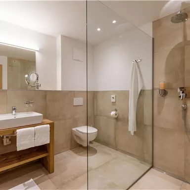 A modern bathroom with a glass shower and a wooden sink. The walls are in neutral colors and there are fluffy towels.