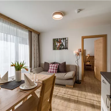 A modern living room with a sofa and a dining area. Bright windows provide plenty of daylight and a cozy atmosphere.