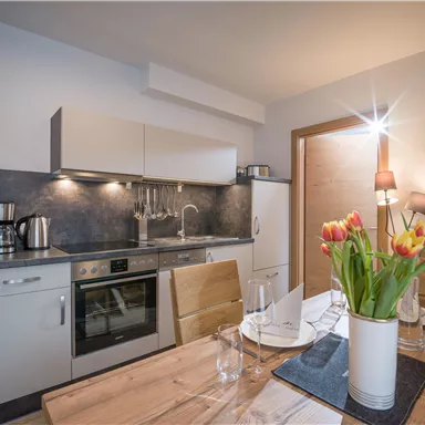 A modern kitchen with wooden details and a dining area. Fresh flowers and a bright atmosphere create coziness.