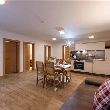 A bright and modern kitchen with a dining area and wooden floor. The living room is cozy furnished with a sofa and a television.