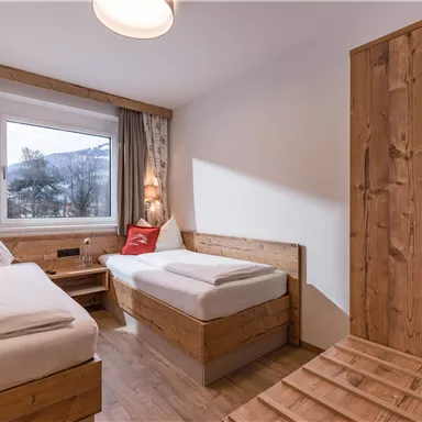 A cozy room with light wood furniture and two beds. The large window offers a view of the landscape outside.