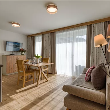 A modern living room with a dining table, chairs, and a comfortable sofa. Large windows let in plenty of light and showcase a bright, inviting space.