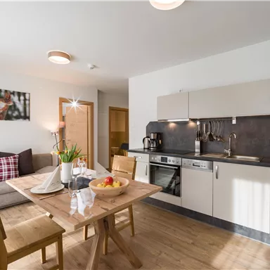 A modern kitchen with a dining area and a cozy living room. There is a table with fresh fruit and a well-equipped kitchen unit.