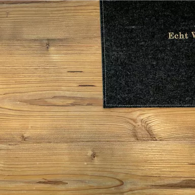 A wooden floor with a dark doormat. The mat has the inscription "Echt Woods" in golden letters.