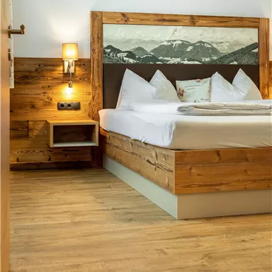 A cozy bedroom with a wooden bed and modern pillows. The room has a warm atmosphere and a natural wooden floor.