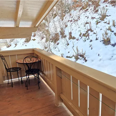 Ein kleiner Balkon mit einem Tisch und zwei Stühlen. Im Hintergrund liegen Schnee und eine bewachsene Fläche.