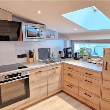 Eine moderne Küche mit Holzschränken und Geräten. Ein Fenster mit Dachflächenfenster sorgt für viel Licht.