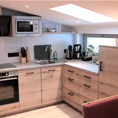 Eine moderne Küche mit Holzoberflächen und neuen Geräten. Sie verfügt über einen Herd, eine Spüle und eine Mikrowelle, sowie einen Blick ins Freie.