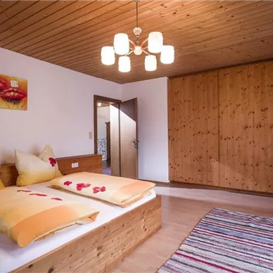 Ein gemütliches Schlafzimmer mit einem Holzbetten und weichen Kissen. Die Wände sind warm und die Decke ist mit Holzpanelen verkleidet.