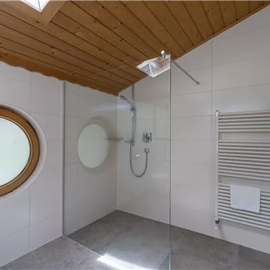 Eine moderne Dusche in einem stilvollen Badezimmer. Die runde Fensteröffnung sorgt für eine angenehme Lichtatmosphäre.