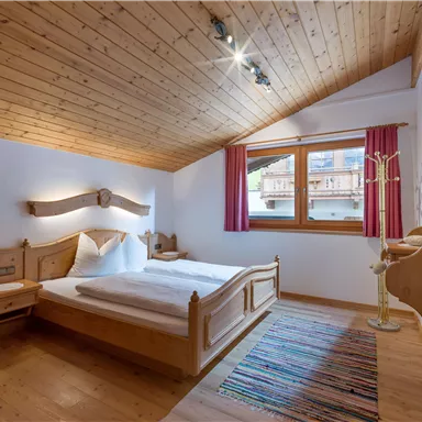 Ein gemütliches Schlafzimmer mit Holzvertäfelungen und einem großen Fenster. Das Zimmer ist hell und freundlich eingerichtet, mit einem Bett und einem bunten Teppich.